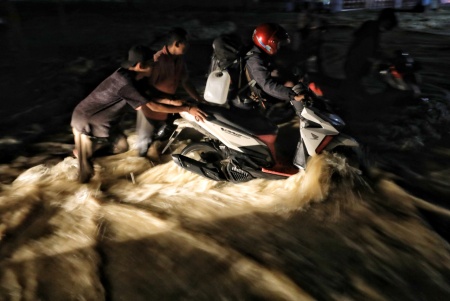 Warga Bantu Pengendara Sepeda Motor Melewati Arus Banjir